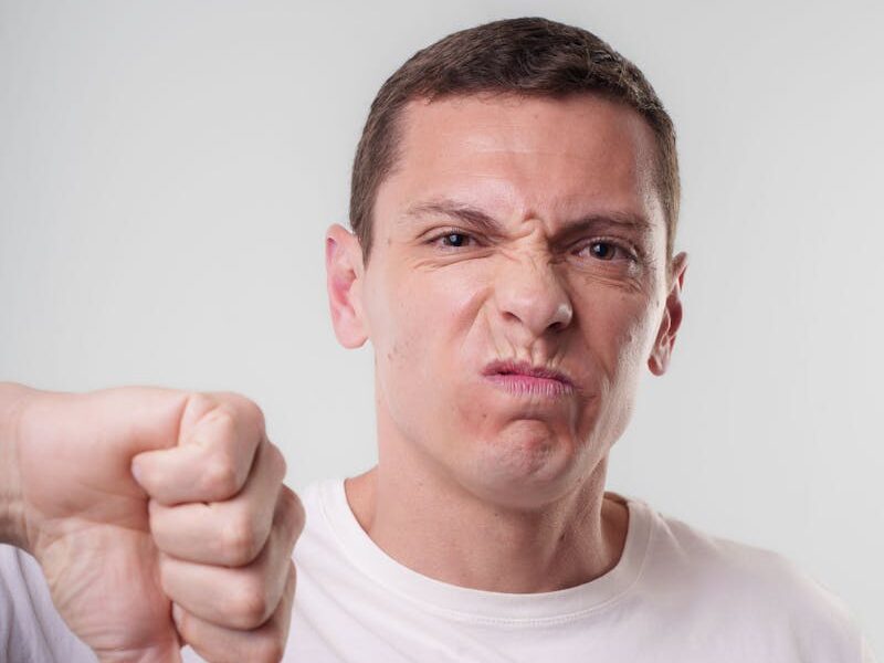 Adult male making a thumbs down gesture with a displeased expression indoors.