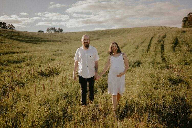 Happy couple in nature, embraced and expecting, under a clear sky.