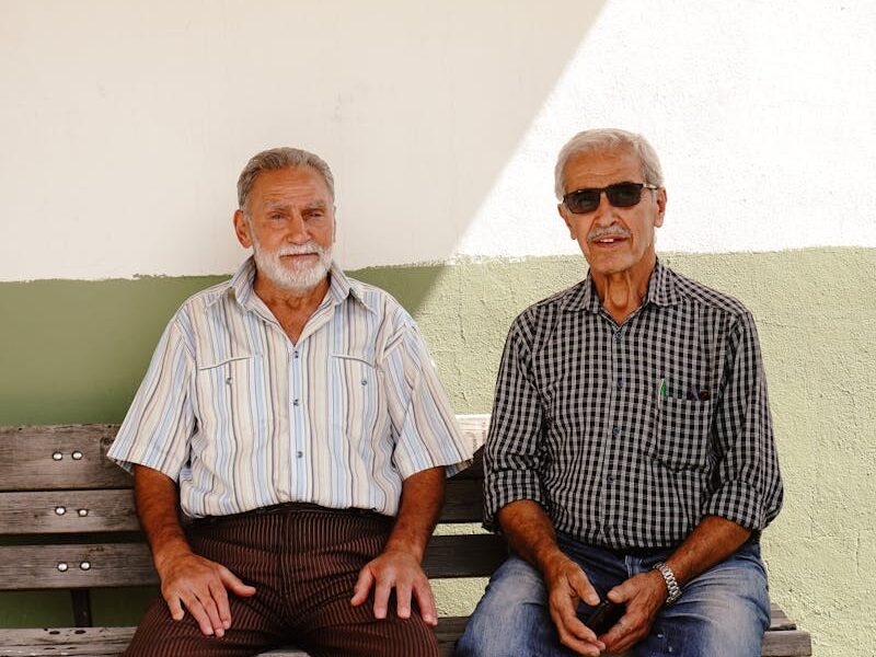 Two senior men sitting on a bench enjoying a sunny day outside.