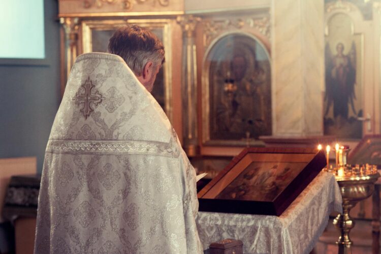 A priest leads a ceremony in a beautifully adorned chapel with icons and candles.