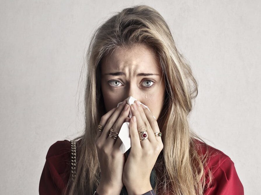 Portrait of a woman sneezing with a tissue, depicting flu symptoms.