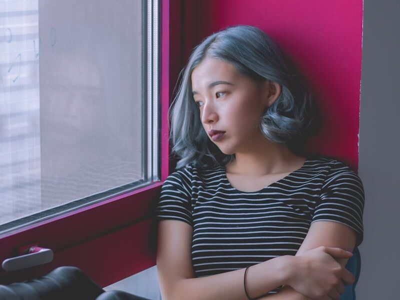 A woman sits by a window, deep in thought, conveying solitude.