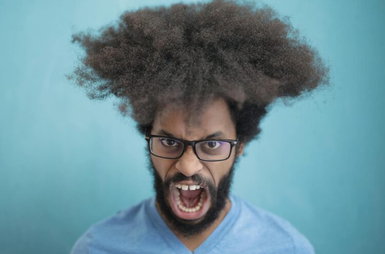 Portrait of a man with afro hair wearing eyeglasses, expressing emotion against a blue background.