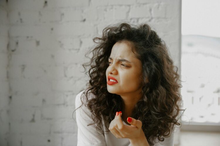 A brunette woman showing an expression of disgust against a brick wall.
