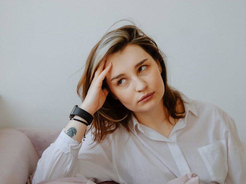 Thoughtful woman in casual attire showing stress indoors, captured in natural light.
