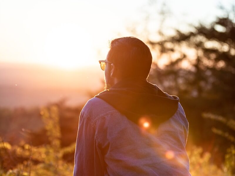 woman in white shirt and sunglasses sitting on brown wooden bench during sunset