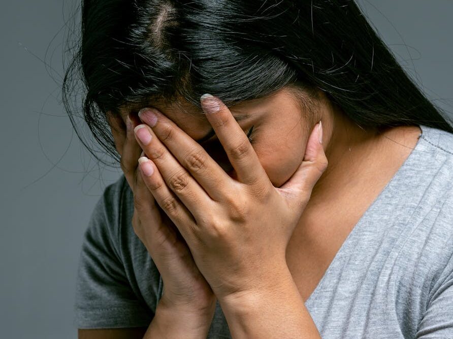 A woman hides her face in hands showing deep emotion and sadness in a studio setting.