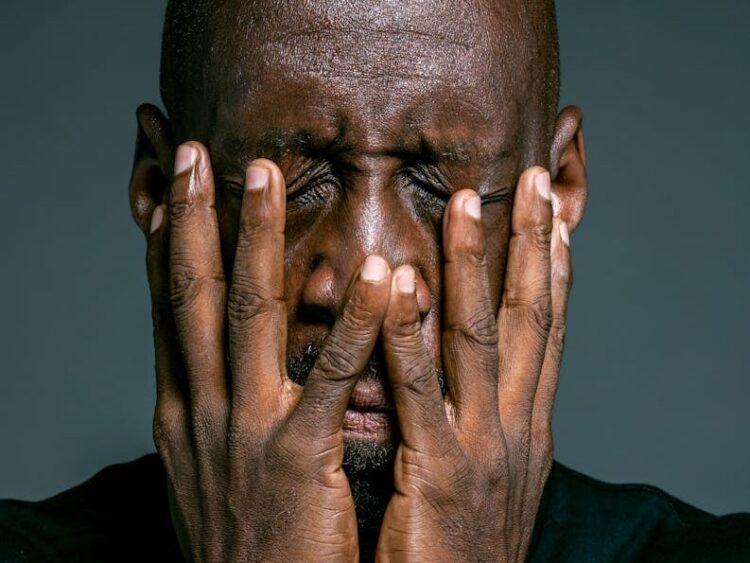 Portrait of a stressed African American man with hands on face expressing frustration.