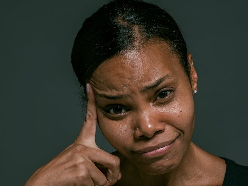 Close-up portrait of an African American woman in a black v-neck shirt with a thoughtful expression.