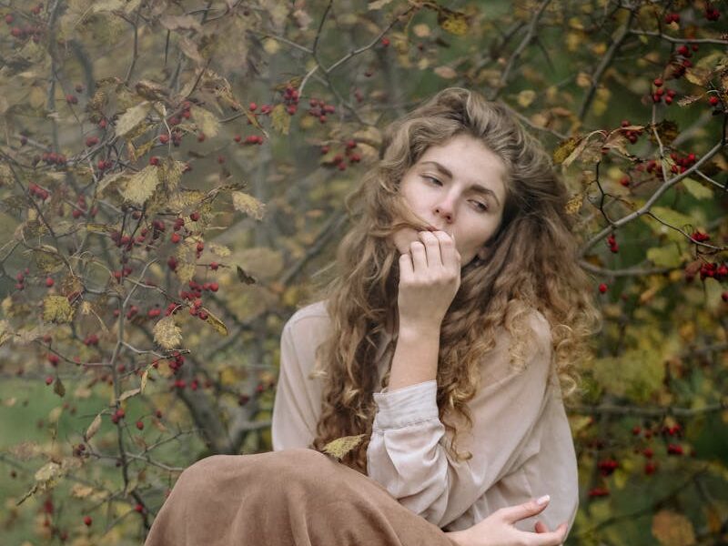 Thoughtful woman sitting on a tree stump in an autumnal forest, lost in deep reflection.