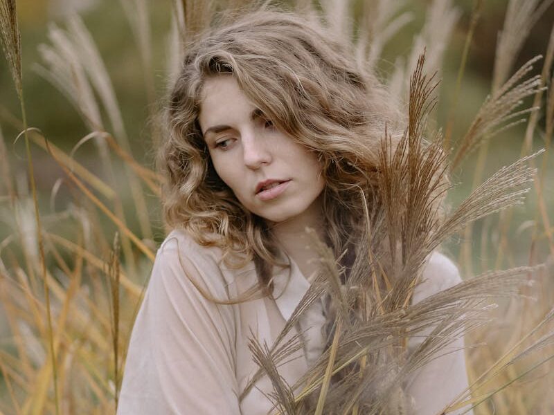 Thoughtful woman in wheat field, embracing autumn's beauty.