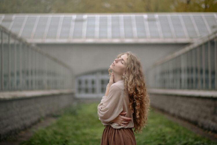 Serene woman in a greenhouse corridor, in deep thought with gentle lighting.