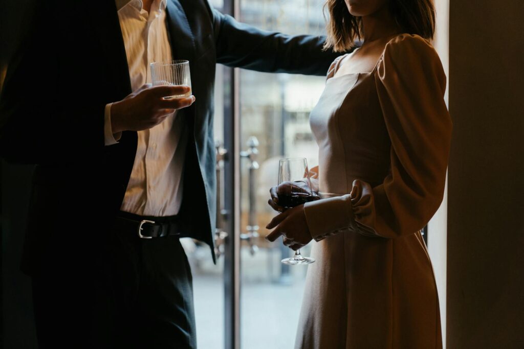 A sophisticated couple in formal attire holding drinks in a moody restaurant atmosphere.