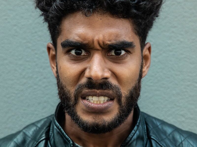 Portrait of a bearded man with curly hair showing an intense facial expression wearing a leather jacket.