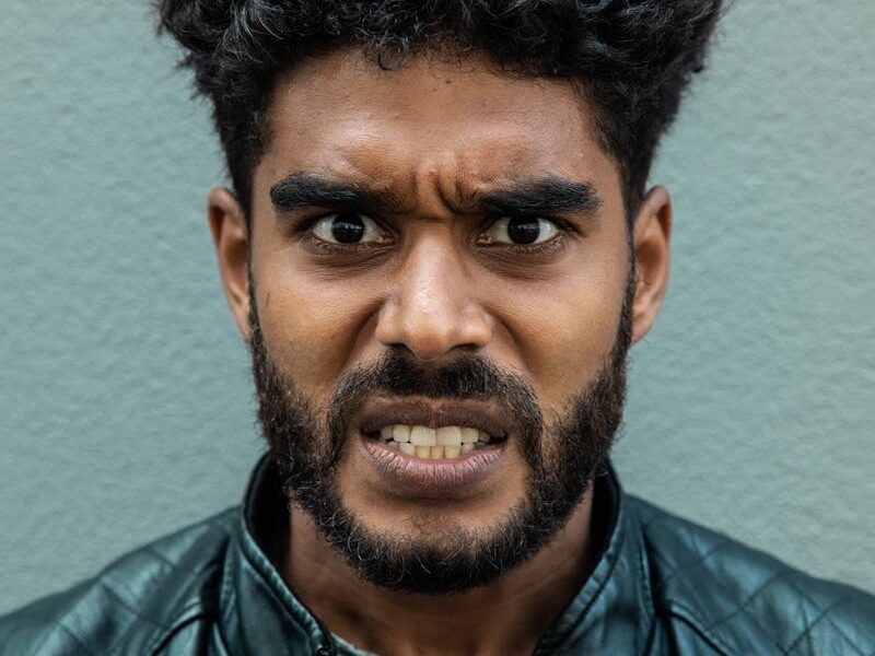 Portrait of a bearded man with curly hair showing an intense facial expression wearing a leather jacket.