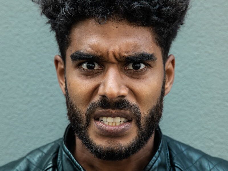 Portrait of a bearded man with curly hair showing an intense facial expression wearing a leather jacket.