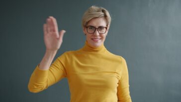 Woman in yellow turtleneck waving hello