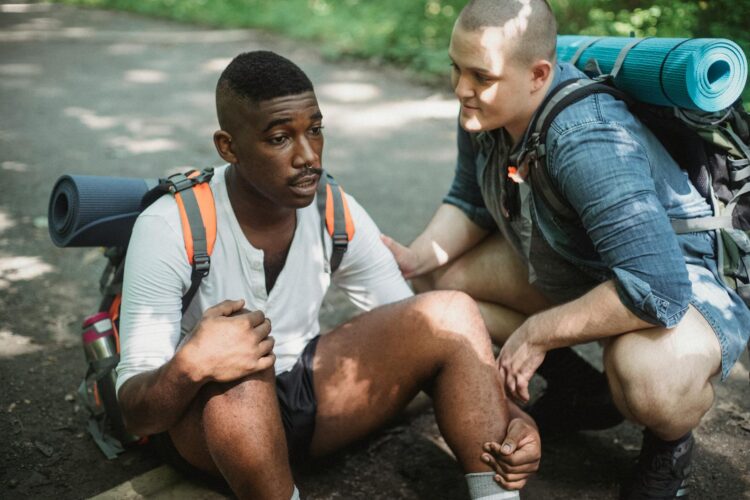 Two male backpackers taking a break from hiking, sitting and discussing on a forest trail.
