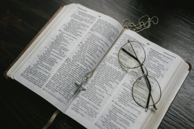 An open Bible with eyeglasses and a cross necklace resting on its pages, symbolizing faith and reflection.