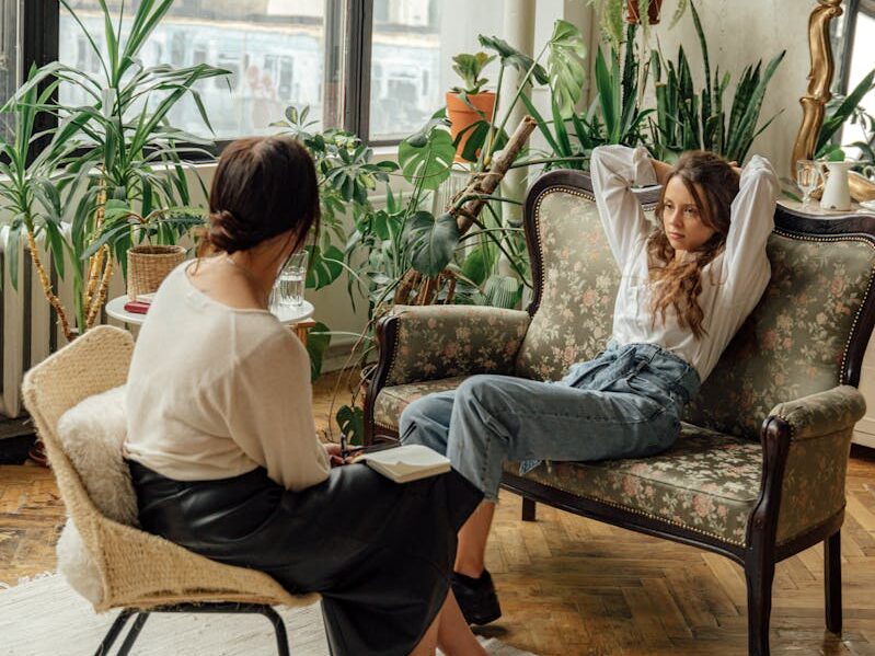 Two women engaged in a counseling session in a cozy, plant-filled living room.