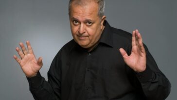 Studio portrait of an older man with a playful gesture in a black shirt.
