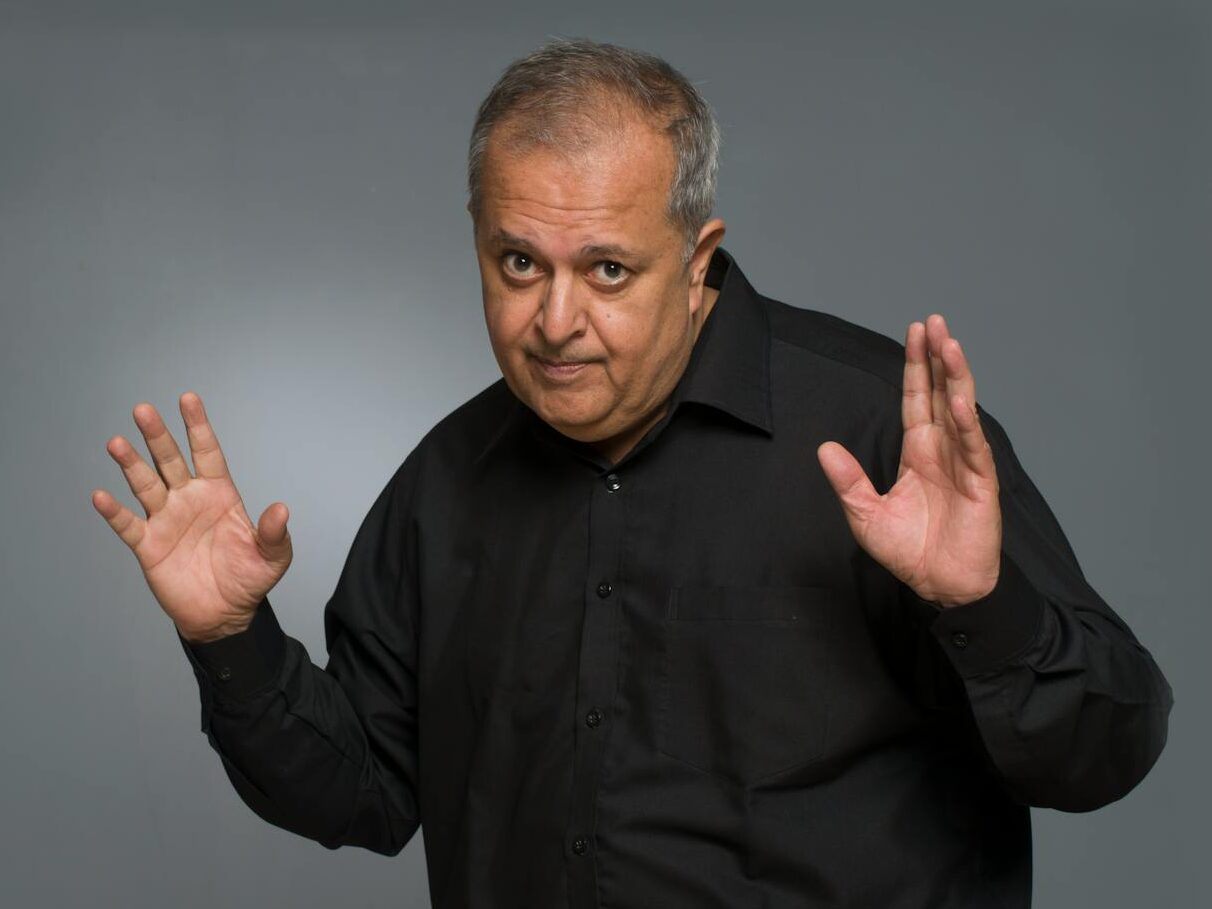 Studio portrait of an older man with a playful gesture in a black shirt.