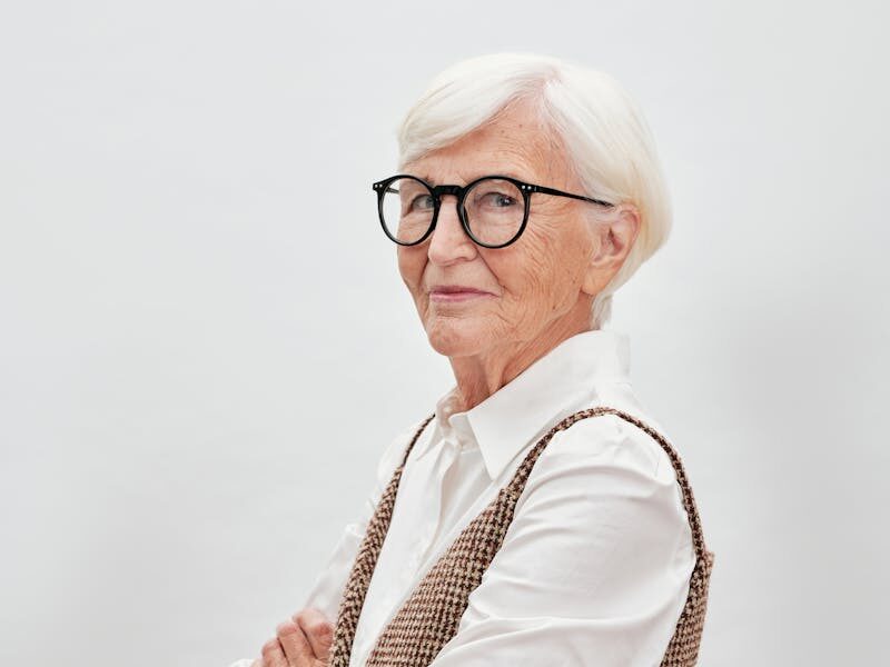 Elegant senior woman with white hair and eyeglasses, posing confidently in a stylish outfit.