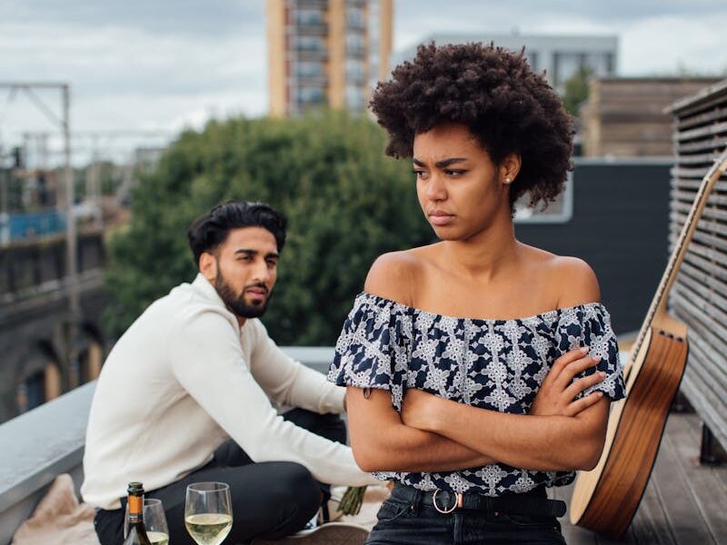 An upset couple having a picnic on a rooftop, with an afro-haired woman sitting with arms crossed.
