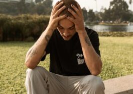A young man sits on a ledge outdoors, appearing deep in thought and contemplation.