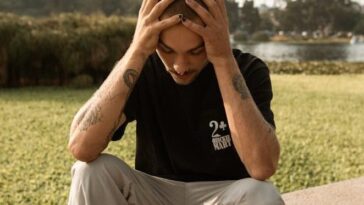 A young man sits on a ledge outdoors, appearing deep in thought and contemplation.