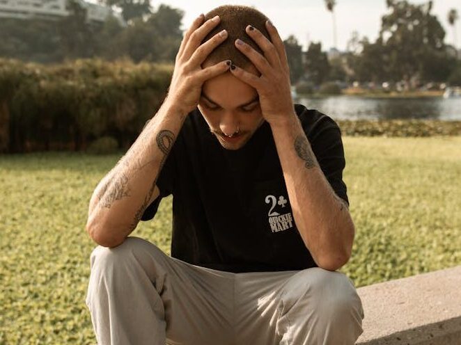 A young man sits on a ledge outdoors, appearing deep in thought and contemplation.