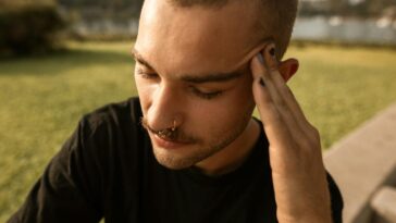 A young man feeling stressed and anxious while sitting outdoors in a park setting.