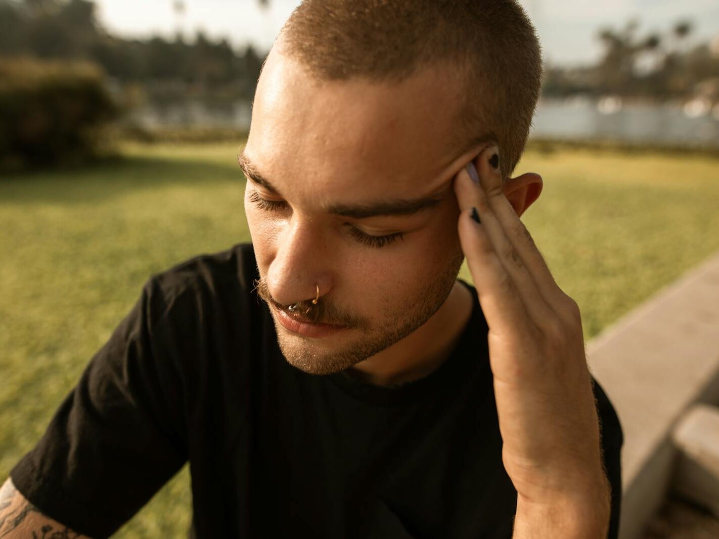 A young man feeling stressed and anxious while sitting outdoors in a park setting.