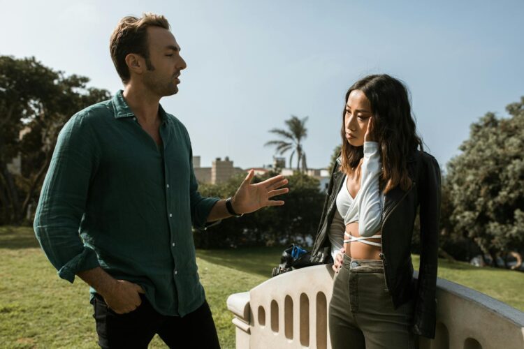 A couple engaging in a serious conversation outdoors in a sunny park setting.