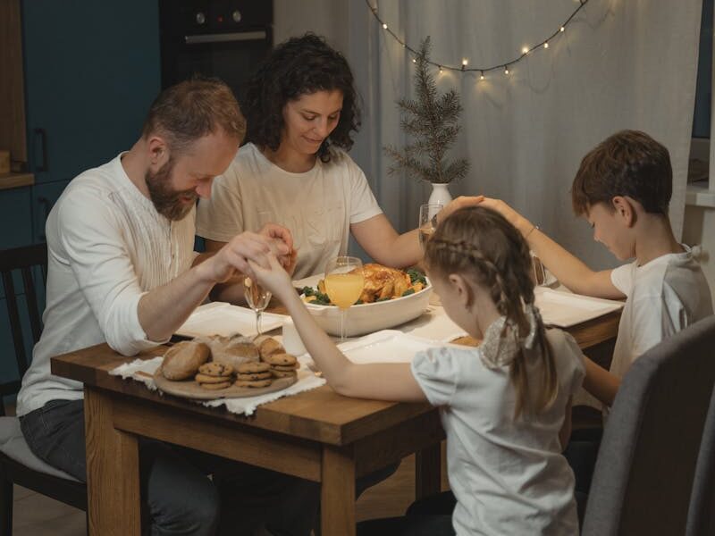 A family holding hands and praying around a festive dinner table set with food and decorations.