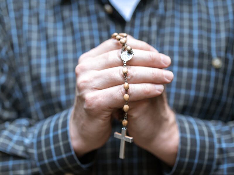 Close-up of a man holding rosary beads in prayer. Focus on faith and contemplation.