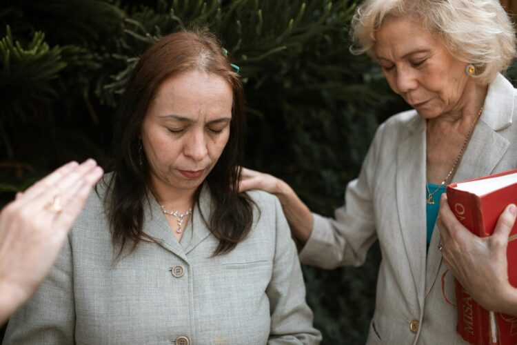 Women praying outdoors, embracing faith and spirituality together intimately.
