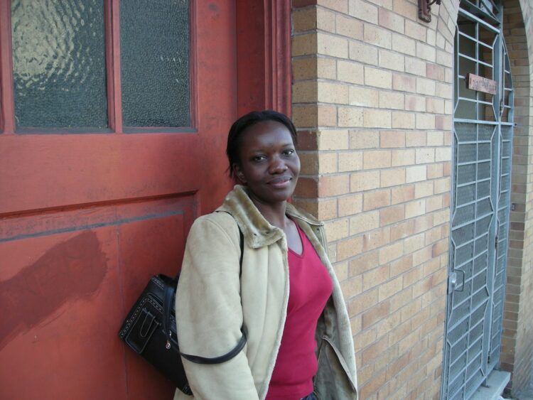 woman in beige coat standing near red wooden door