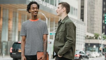 Smiling multiracial friends in casual clothes standing on street near roadway and talking against buildings in city in daytime