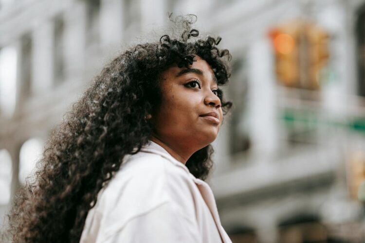 Portrait of a young woman with curly hair standing in a city, exuding confidence and independence.