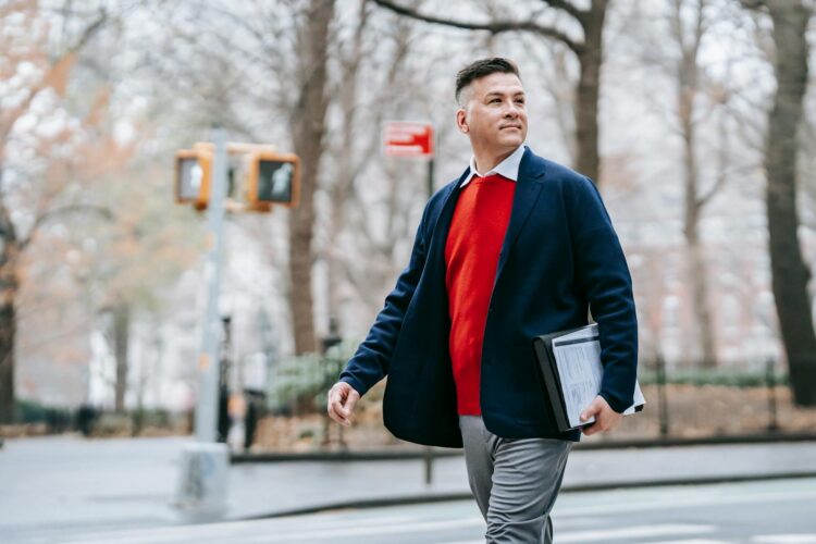 Stylish man walking confidently in an autumn park carrying documents and wearing business attire.