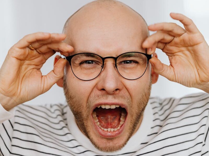 Bald man wearing striped shirt and eyeglasses, expressing anger or frustration.