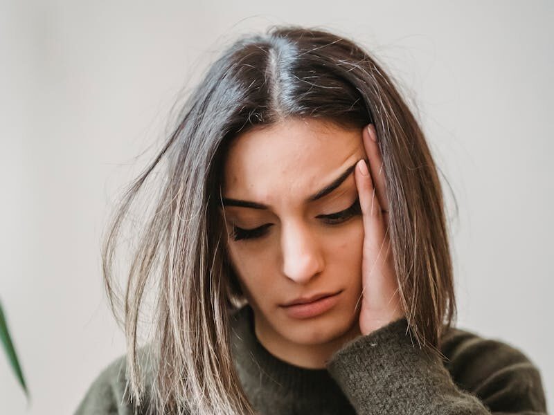 Unhappy female in casual wear leaning on hand and surfing internet on cellphone while sitting in light room near wall at home