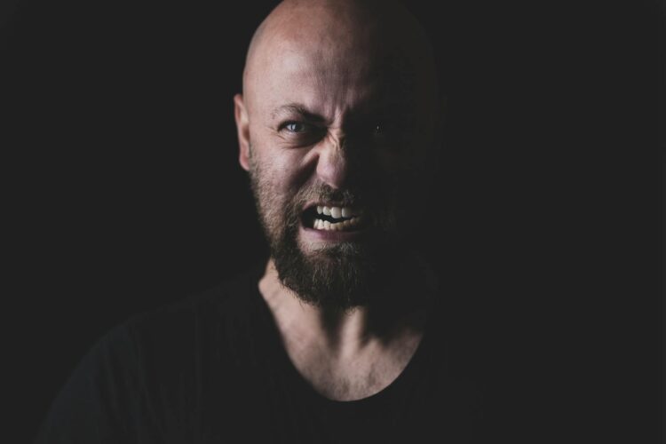 Close-up of a bald and bearded man showing a fierce expression in a dark setting.