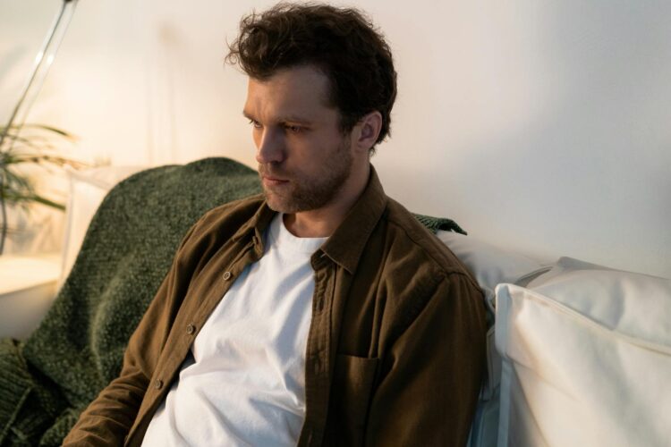 A thoughtful man sitting indoors, reflecting quietly on a sofa in a cozy ambiance.