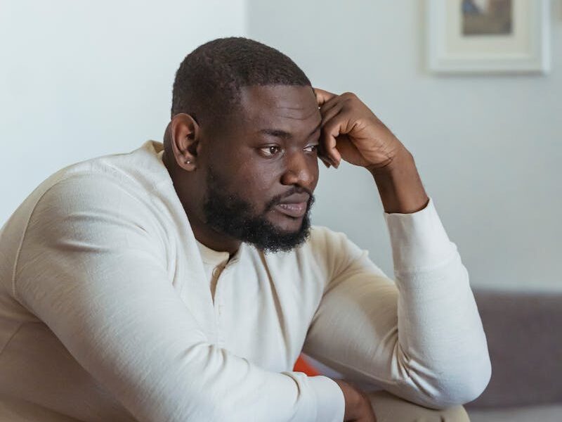A thoughtful adult man sits in a cozy home setting, focused on his laptop.