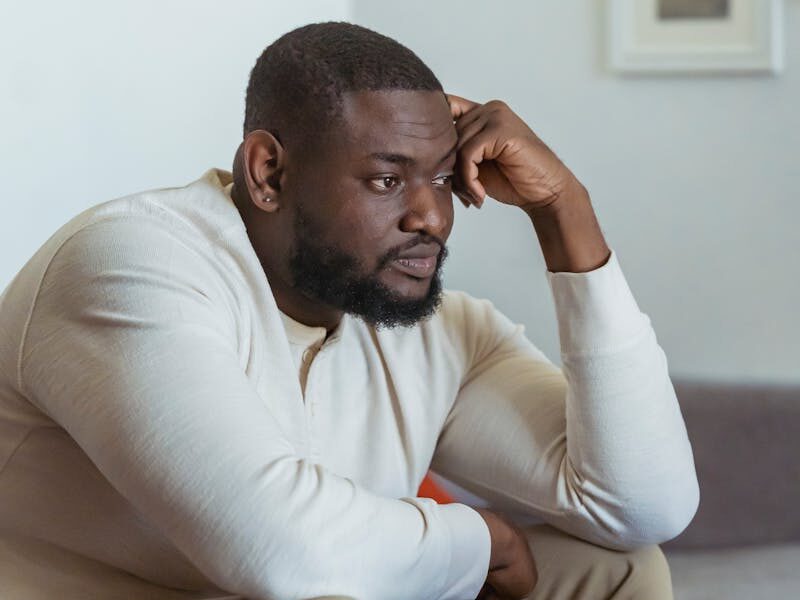 A thoughtful adult man sits in a cozy home setting, focused on his laptop.