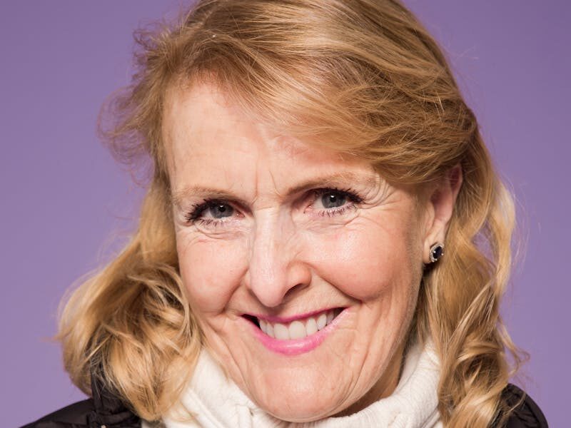 Portrait of a smiling senior woman in casual fashion against a purple background, exuding elegance and warmth.