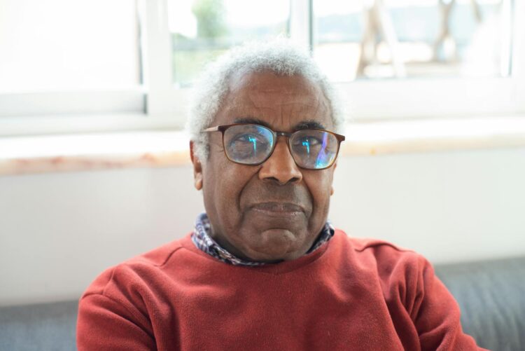 Close-up portrait of a senior man wearing glasses, indoors with natural light.