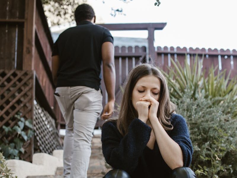 A woman sitting in distress while a man walks away outdoors, capturing emotion and separation.